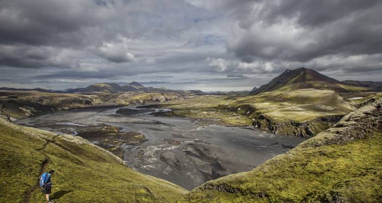 Vasto valle de las tierras altas de Islandia con canales de río trenzados entre crestas verdes y musgosas bajo nubes dramáticas
