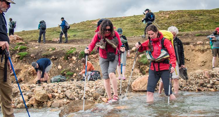 People crossing a rocky stream assisted by walking sticks.