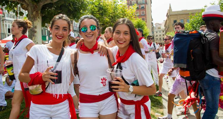 Trois jeunes femmes souriantes à un festival, tenant des boissons.