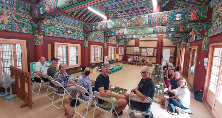 Grupo de personas sentadas dentro de un edificio tradicional coreano con decoración colorida.