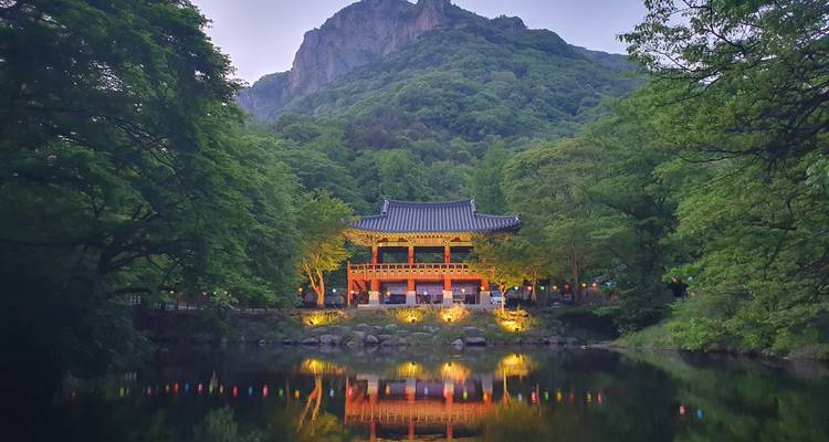 Templo coreano tradicional junto a un lago con montañas de fondo.