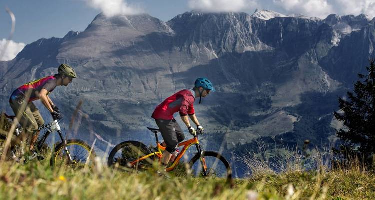 Two people mountain biking with mountainous backdrop