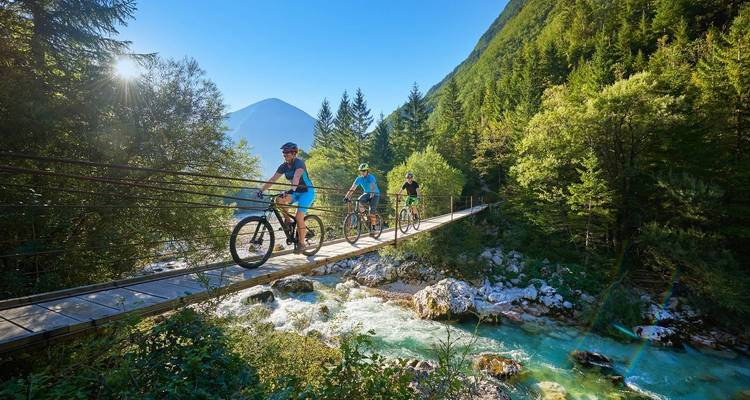 Group biking on a bridge over a river with mountains in the background