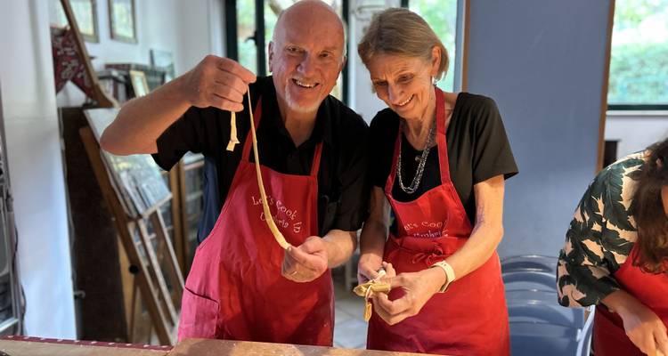 Zwei Personen kochen Nudeln und tragen rote Schürzen.
