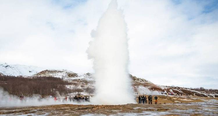 Ein Geysir, der in Island ausbricht, mit Zuschauern ringsum.