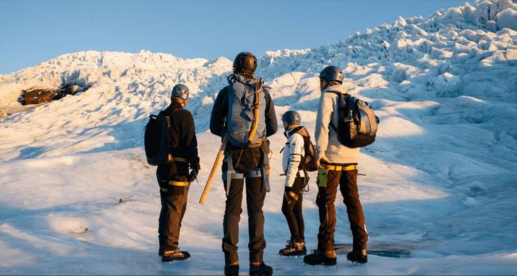 Kleine Gruppe mit Helmen und Eispickeln, die auf einem hell leuchtenden gefrorenen Gletscher in Island während des Sonnenaufgangslichts steht