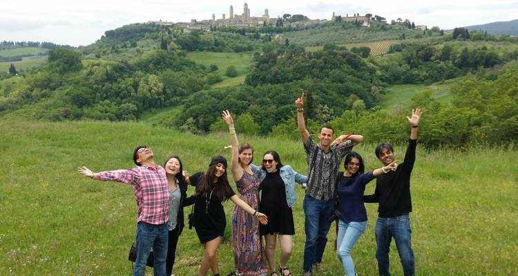 Groep vrolijke mensen poseert in een grasveld met een stad op een heuvel op de achtergrond.