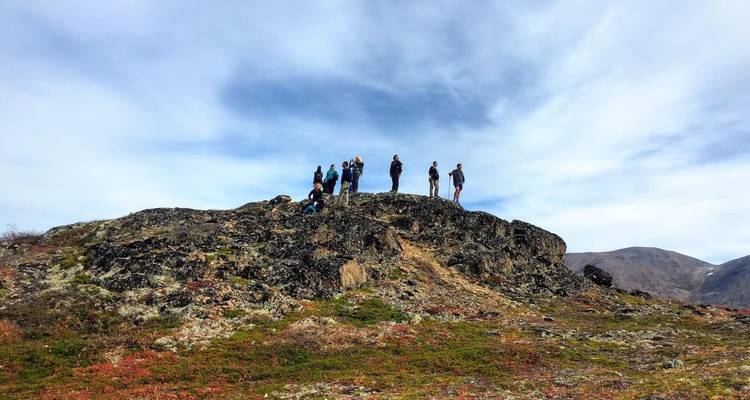 A group of people standing on a rocky outcrop with a blue sky background.