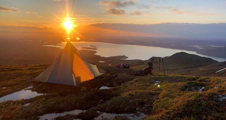 A beautiful tent set up on a hillside with a stunning view of a sunset over a lake.