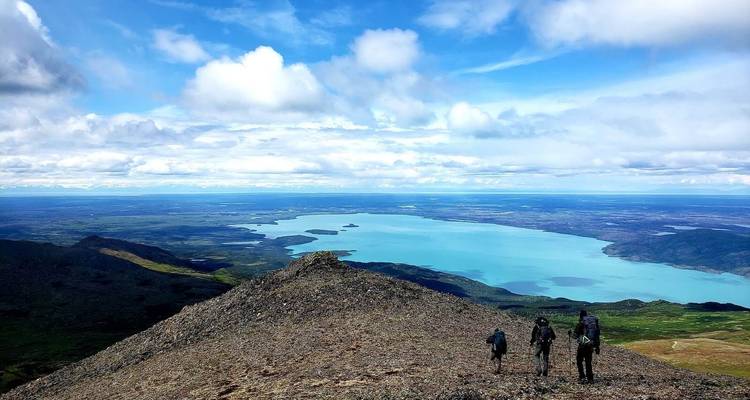 Three people hiking down a rocky slope overlooking a lake and vast landscape.