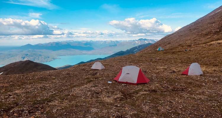 Campsite on a mountain overlooking a blue lake under a bright sky.