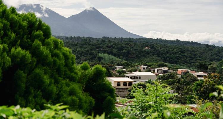 Deux pics volcaniques jumeaux s'élèvent au-delà d'une vallée verdoyante parsemée de maisons de village et d'arbres luxuriants.