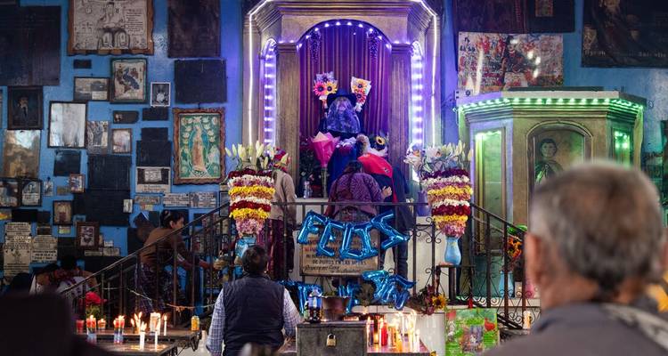 Intérieur animé d'un sanctuaire orné de néons, de fleurs et de fidèles priant devant une effigie décorée.