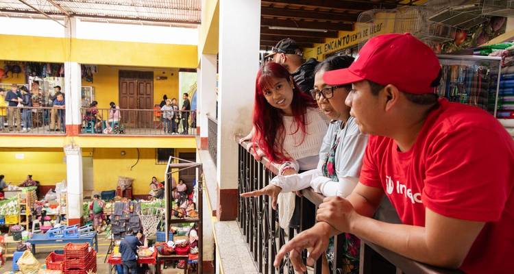 Travellers lean over a balcony inside a lively indoor market filled with fruit, vegetables and local vendors.