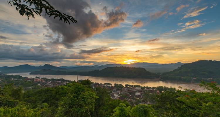Vue panoramique d'une rivière avec des montagnes environnantes sous un ciel de coucher de soleil dramatique.