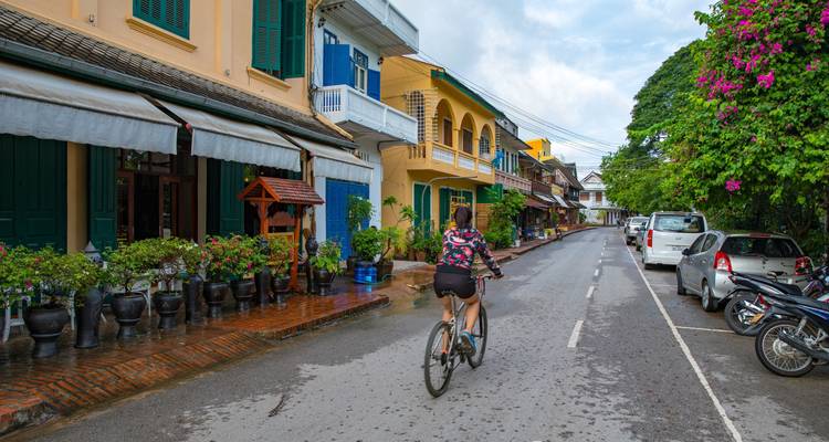 Scène de rue avec une personne à vélo, entourée de bâtiments coloniaux.