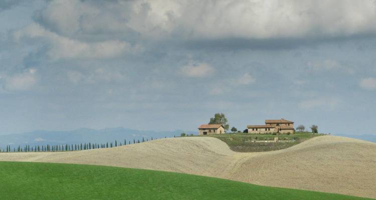 Colinas ondulantes toscanas con una casa de campo solitaria y filas de cipreses bajo un cielo nublado