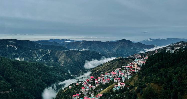Vista aérea de un pueblo en la ladera con techos rojos y montañas brumosas.