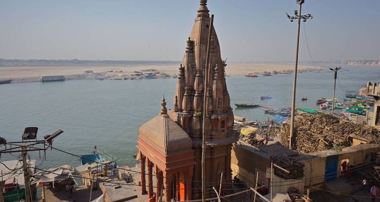 Uitzicht over de Ganges met een hoge tempelspits en boten afgemeerd langs de ghats