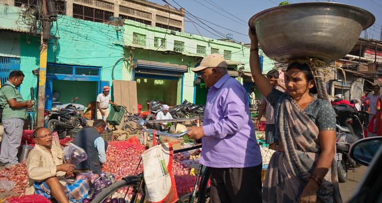 Marché indien de légumes animé avec des vendeurs, des acheteurs et des motos au milieu de produits colorés.