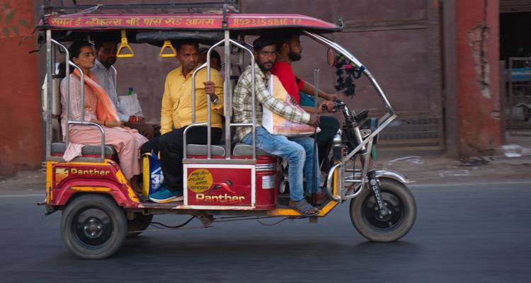 Un coloré tuk-tuk indien bondé de passagers dépasse rapidement un mur de ville usé par le temps.