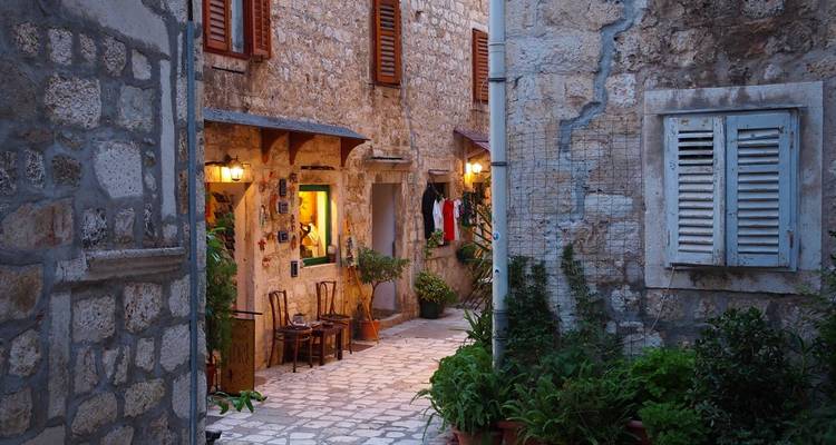 Charmante ruelle avec des murs en pierre et des chaises alignées dans un village pittoresque.
