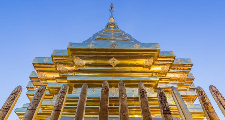 Goldene Stupa durch einen Holzzaun betrachtet vor einem blauen Himmel.