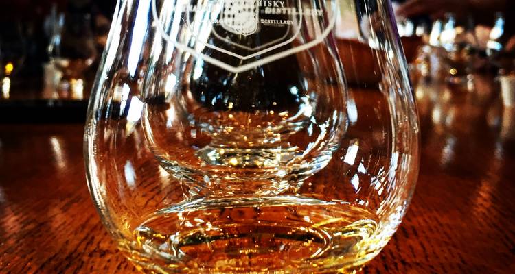 Primer plano de un vaso de whisky con reflejos sobre una mesa de madera.