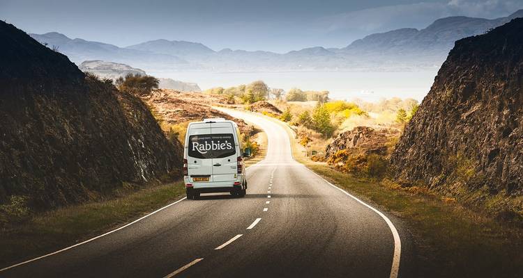 Une camionnette roulant le long d'une route pittoresque avec des montagnes et un lac en arrière-plan.
