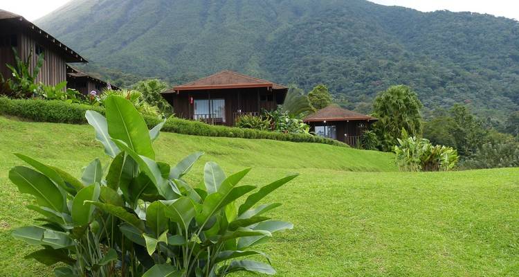 Cabañas de madera acurrucadas en una ladera de césped bien cuidado con colinas cubiertas de selva tropical detrás