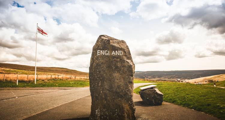 Piedra que marca 'Inglaterra' en el borde de la carretera con bandera.