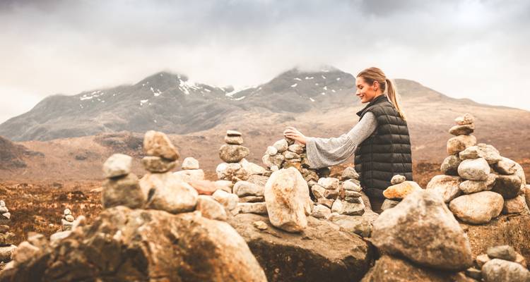 Frau, die einen Steinturm baut, mit einer Berglandschaft im Hintergrund.