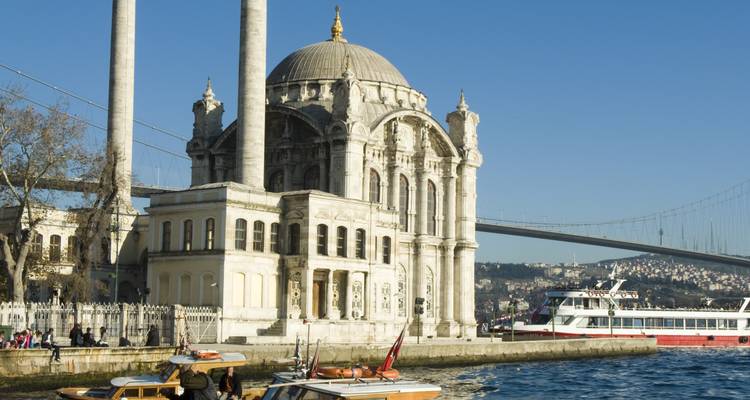 Eine historische Moschee am Wasser mit einer Brücke im Hintergrund.