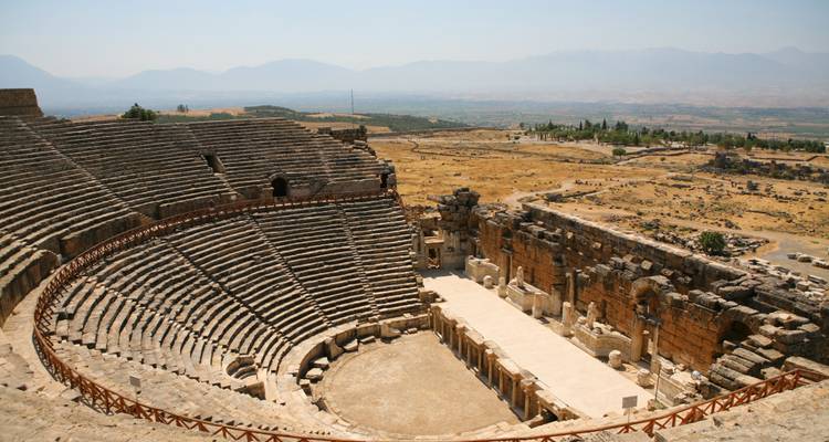Ein antikes Amphitheater mit einer bergigen Landschaft im Hintergrund.