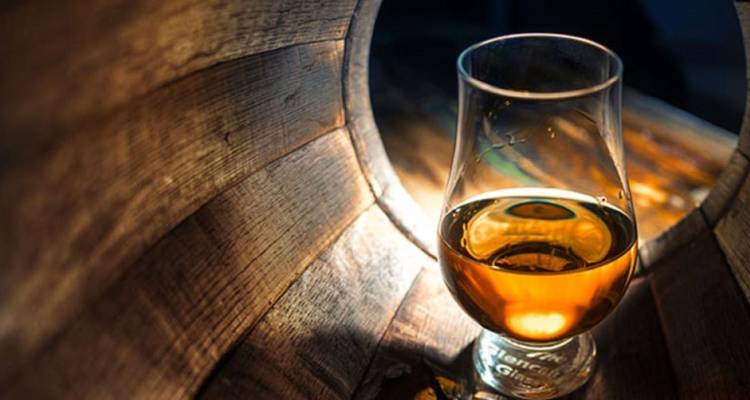 Primer plano de una copa de whisky brillando dentro de un barril de madera, resaltando tonos ámbar.